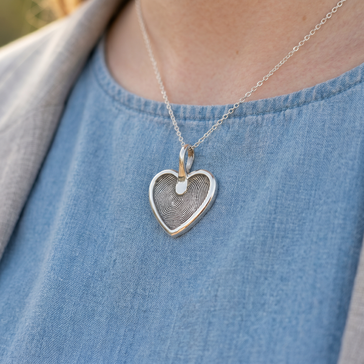 A silver fingerprint heart pendant worn on a fine chain.
